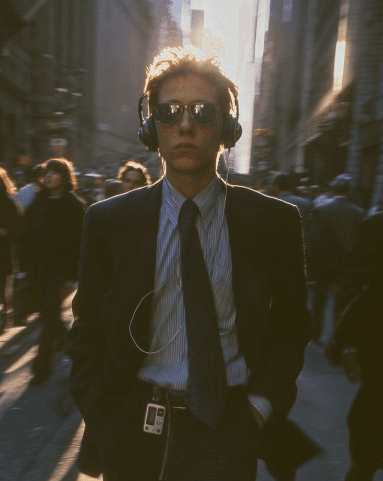 Joven de traje y audífonos caminando por el distrito financiero a contraluz